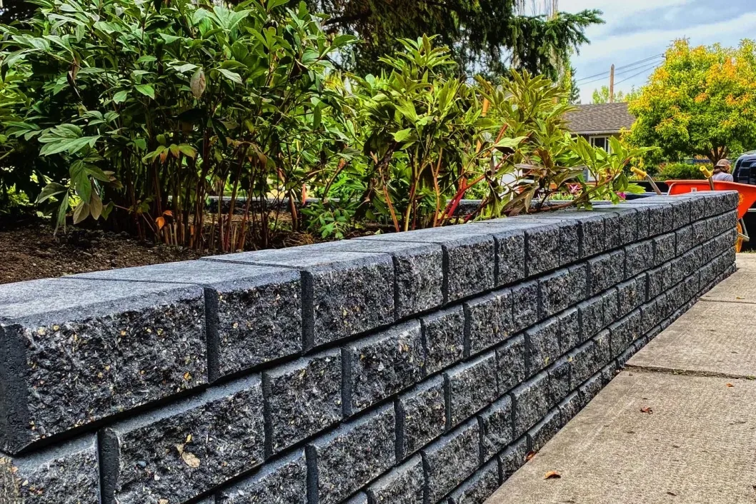 Dark granite block retaining wall with lush shrubs framing a Calgary garden bed, All The Moore Landscaping